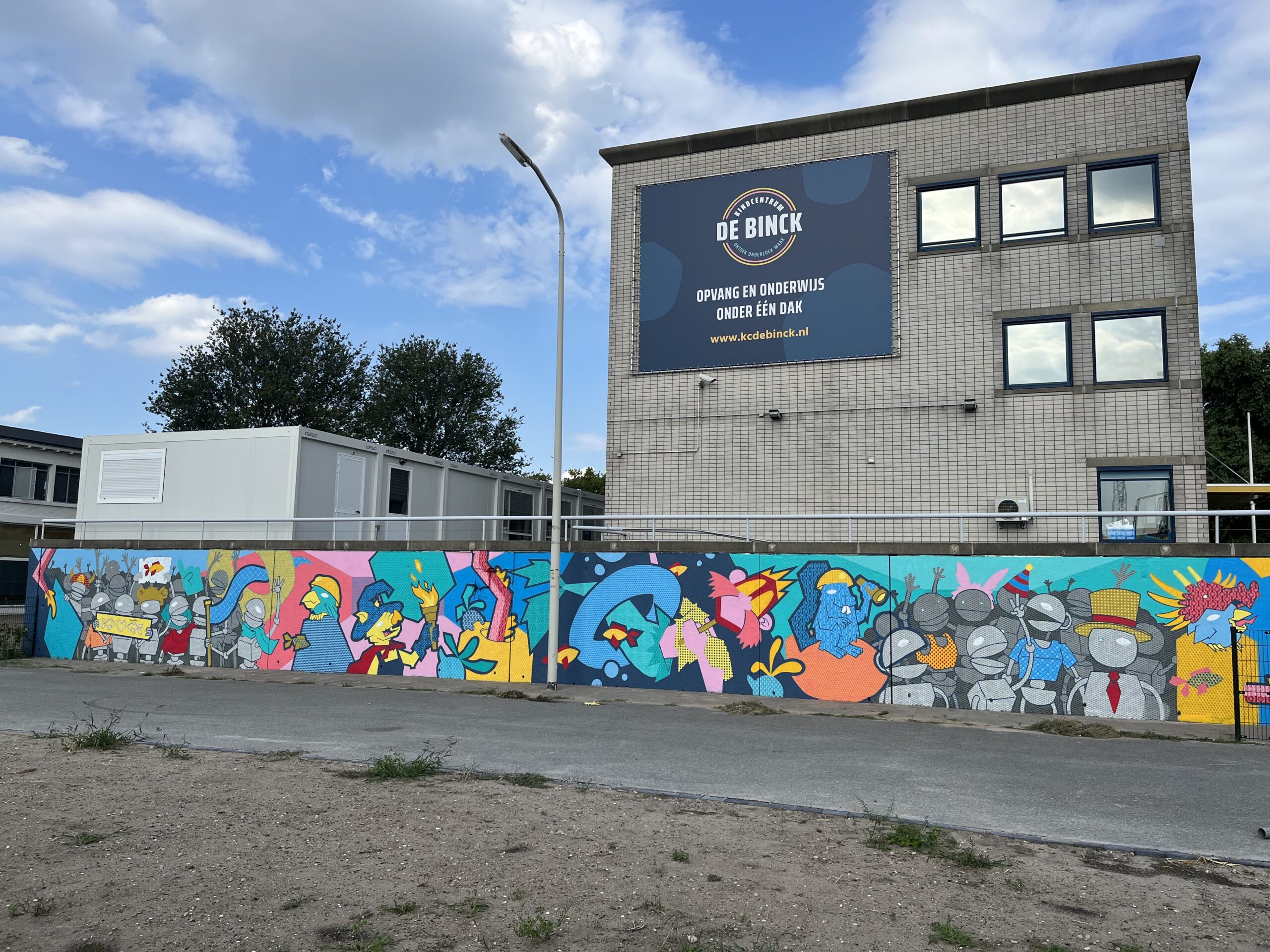 Het gebouw van kindcentrum De Binck, met op de voorgrond de straat met een schutting met graffiti.