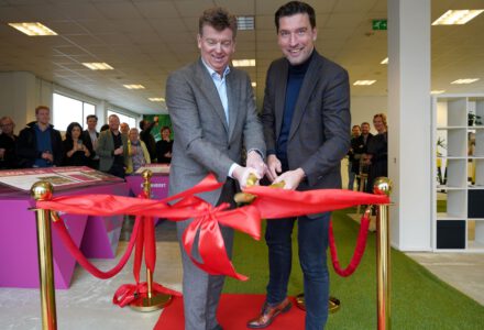 Hans Meurs en wethouder Robert van Asten (rechts) knippen een groot rood lint door om het informatiecentrum Binckhorst te openen.