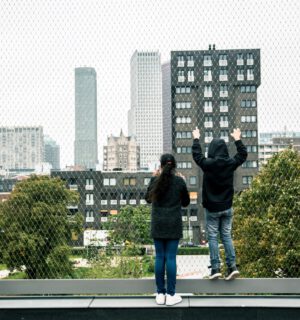 2 kinderen kijken door een gaas naar hoge gebouwen in de verte.